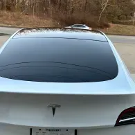 Rear view of a white Tesla sedan with a tinted rear window, parked outdoors.