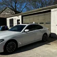 White sedan parked in a driveway in front of a beige garage under a clear blue sky