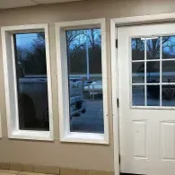 White-framed windows and a door on a beige interior wall, showing cars and trees outside.