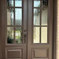 Double front doors with glass panes and beige trim, viewed from outside.