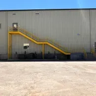 Yellow staircase on a gray industrial building with a large concrete lot in front
