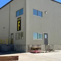 Industrial building exterior with gray metal siding, blue windows, and a concrete loading area