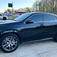Black sedan parked on a concrete driveway, side view, with tinted windows and silver rims.