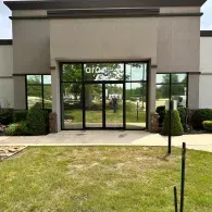 Glass entrance to a beige office building with a grassy lawn in front
