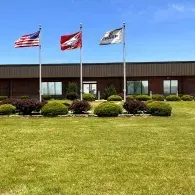 Three flags flying outside a brick building on a sunny day, with a manicured green lawn in front.