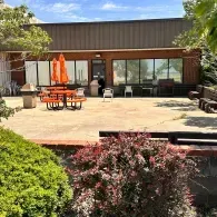 Patio with orange umbrella table, lounge chairs, and sliding glass doors beside greenery