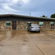 Silver car parked in front of a stone building under a cloudy sky