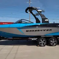 Blue and black WakeSetter wake boat on a trailer outdoors under a clear sky