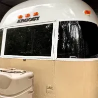 White and beige Airstream trailer front with windows and orange lights under a canopy