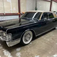 Black classic sedan parked indoors, with chrome trim and whitewall tires.
