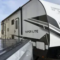White and black Vapor Lite travel trailer parked beside a truck in a lot