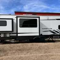 White travel trailer with black trim parked in a dry field under a blue sky