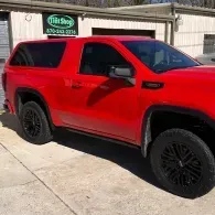 Red pickup truck parked outside a building, with black wheels and tinted windows.