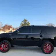 Black SUV with tinted windows and red rims parked on a driveway under a clear blue sky