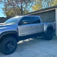 Silver pickup truck parked in a driveway beside a garage under trees