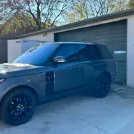 Black SUV parked in front of a garage with a blue cover over the windows.