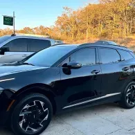 Black sedan parked outdoors beside a silver SUV, with autumn trees in the background
