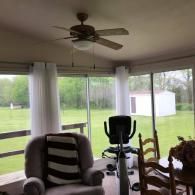 Sunroom with a chair, exercise bike, dining table, ceiling fan, and large windows overlooking a green yard