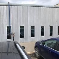Metal-sided building exterior with narrow windows and parked cars in front