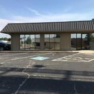 Empty storefront in a strip mall with large windows and an accessible parking space in front
