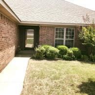 Brick house entrance with front walkway, lawn, shrubs, and a large window under a sloped roof