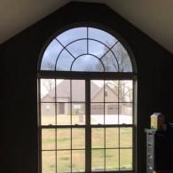Arched window with grid panes overlooking a house and grassy yard