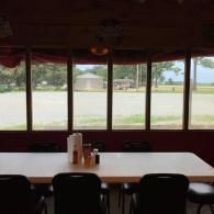 Empty dining area with tables and chairs facing large windows overlooking a bright outdoor view