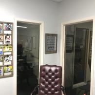 Office hallway with open doors, a tufted brown chair, and framed wall decor.