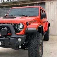 Orange Jeep Wrangler Rubicon with off-road tires parked beside a building