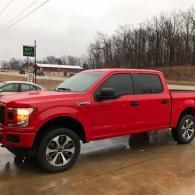 Red pickup truck parked on a wet roadside under an overcast sky