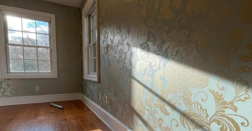 A room with hardwood floors and a window with a patterned wallpaper on the wall.