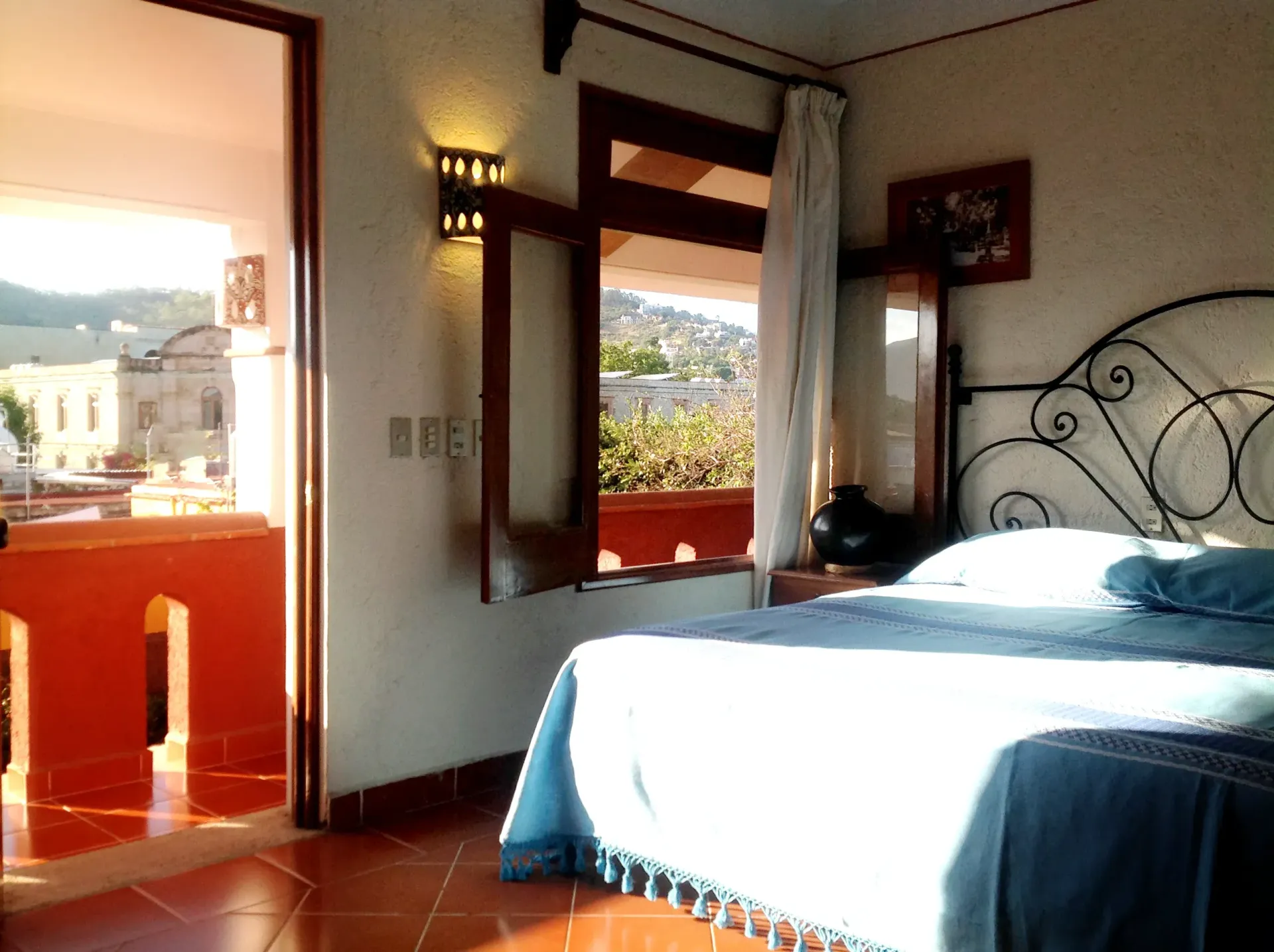 Una luminosa habitación de hotel con cama y ropa de cama, con acceso a una soleada terraza con vistas a los edificios.