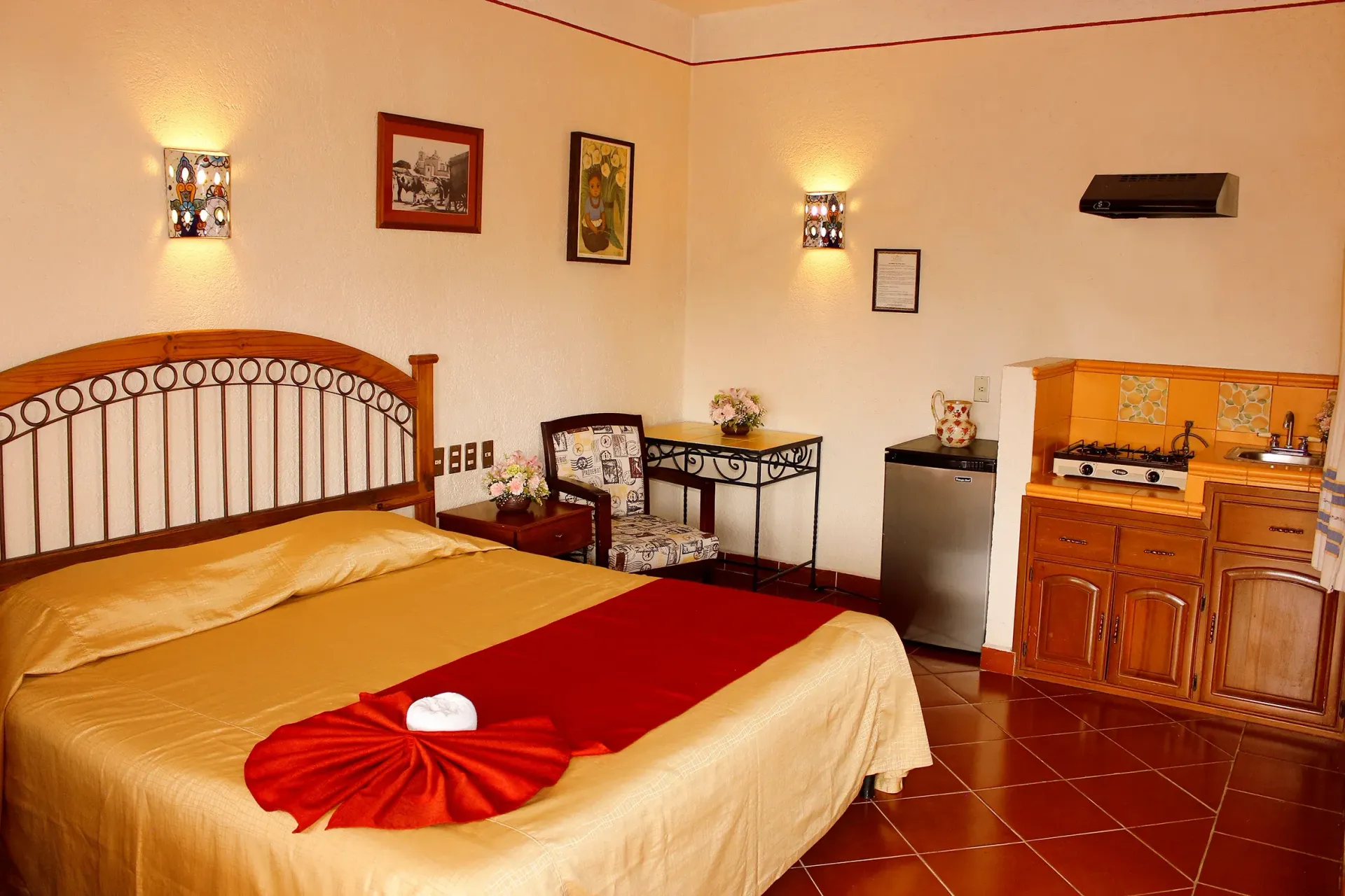 Una habitación de hotel con una cama con una colcha dorada y una alfombra roja, un cabecero de madera.