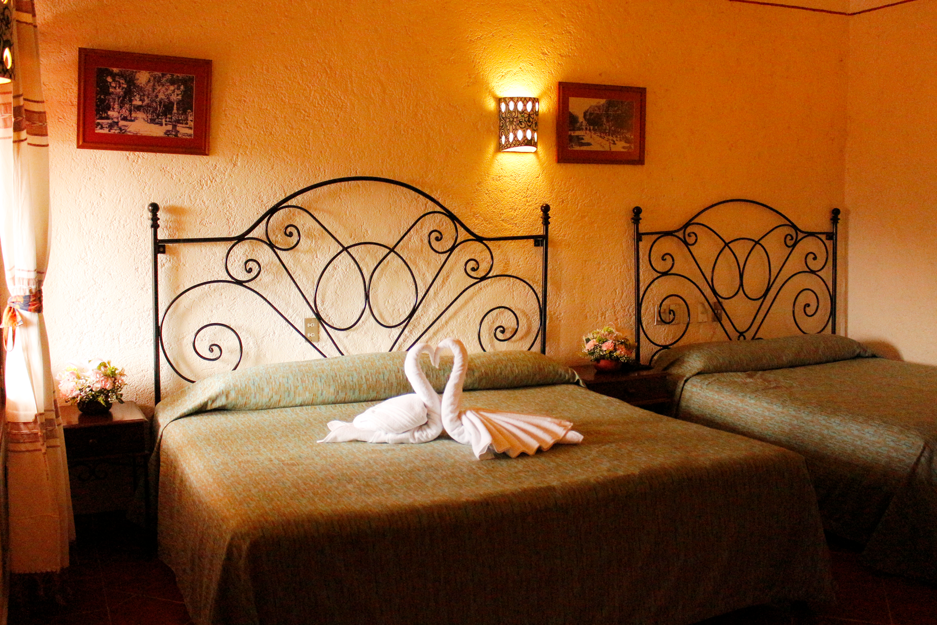 Una habitación de hotel con dos camas con cabeceros de metal ornamentados a juego, colchas verdes.