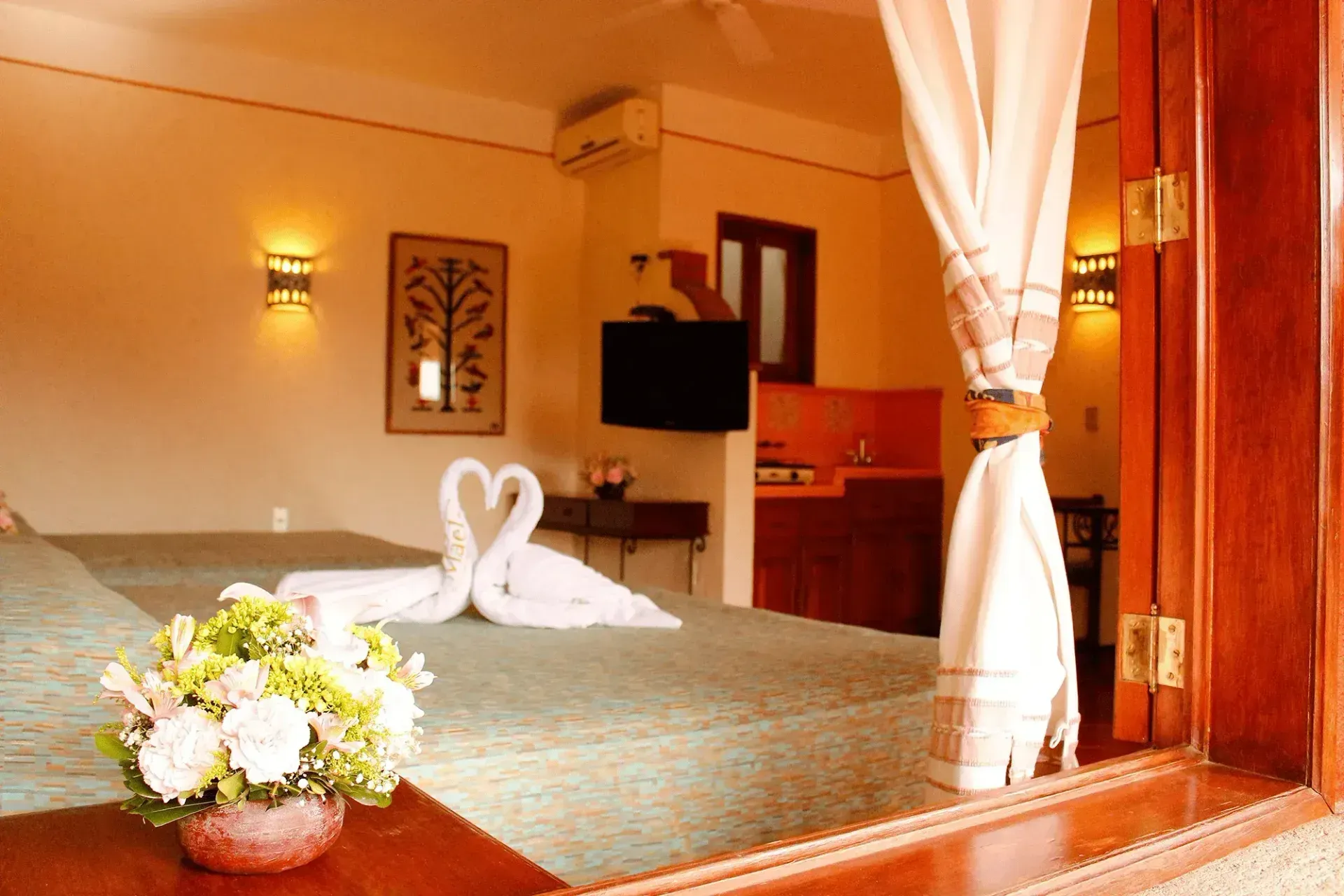 A bedroom with a green bedspread, a black wrought-iron headboard, and two towel swans arranged in the center.