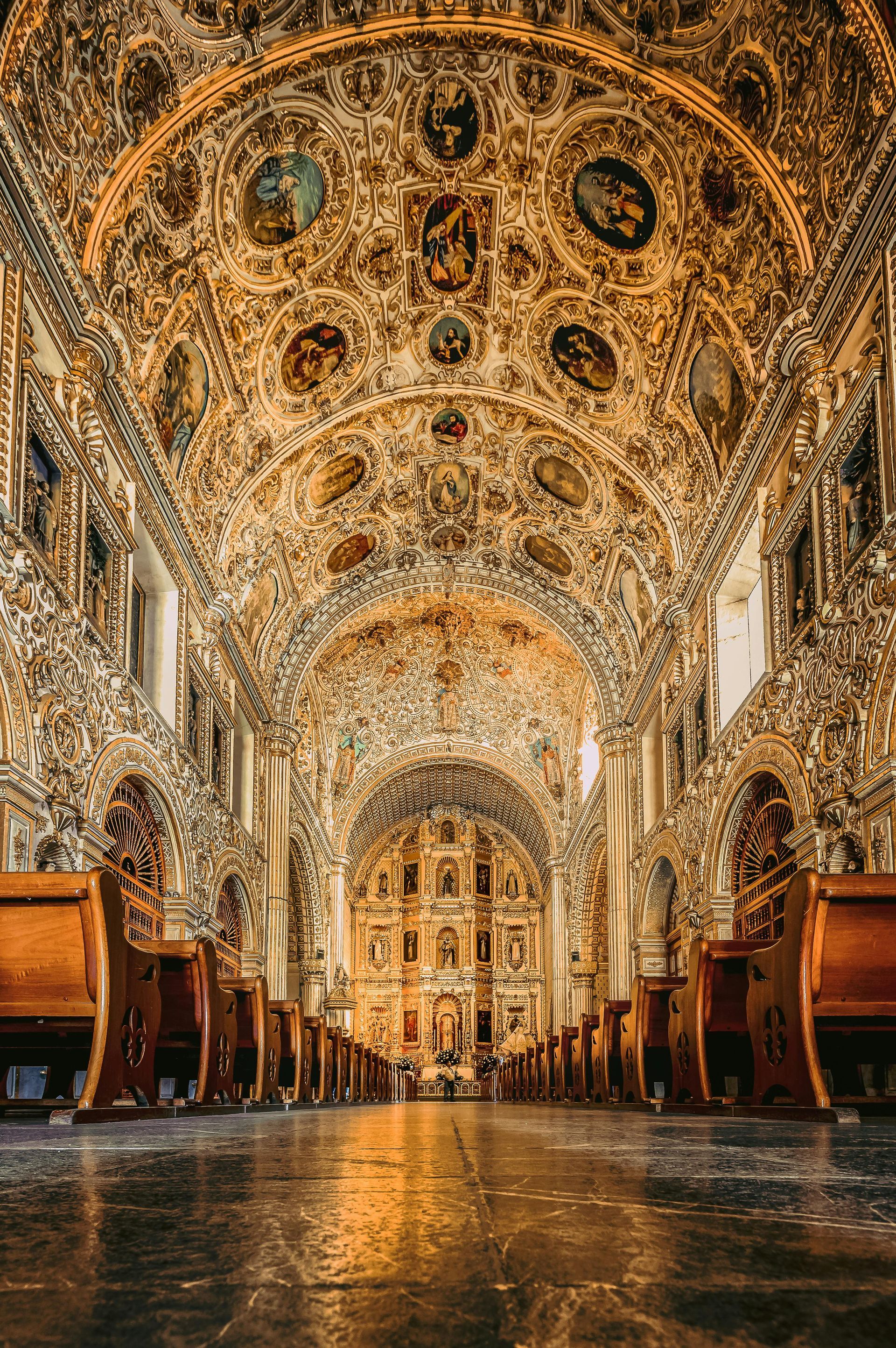 Vista desde un ángulo bajo del interior de una gran catedral con techos ornamentados y dorados.
