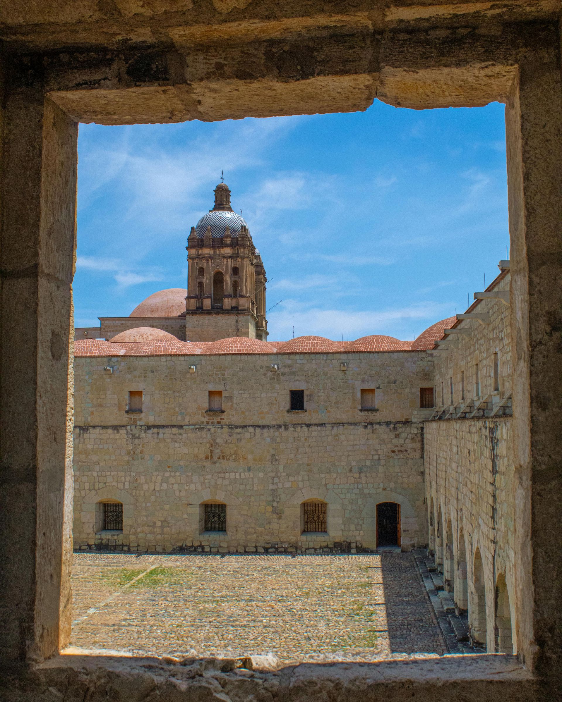Vista desde una ventana con marco de piedra del patio de un antiguo monasterio con una cúpula central bajo.
