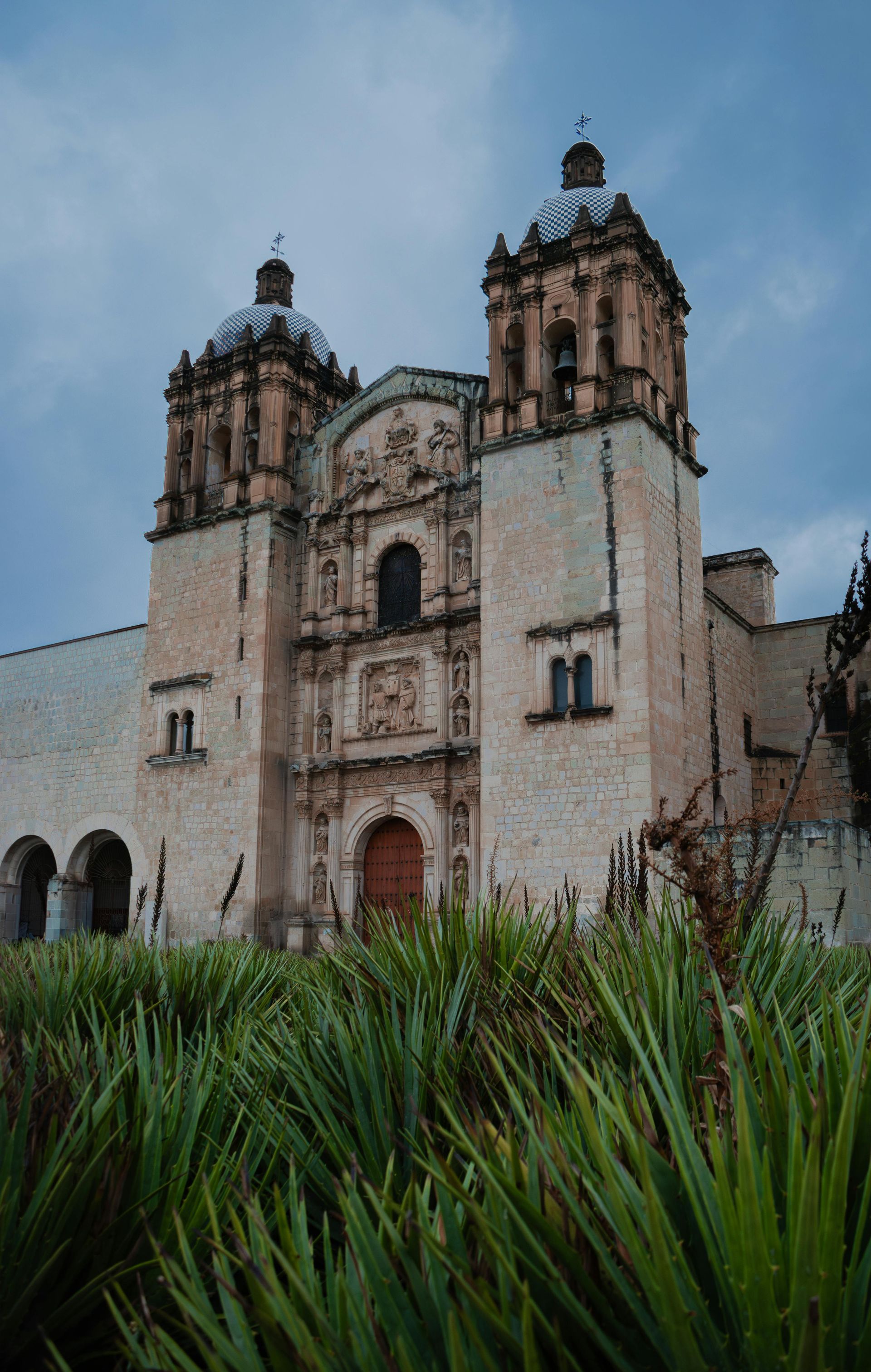 Vista desde un ángulo bajo de la ornamentada fachada de piedra y los dos campanarios de una iglesia de estilo colonial.