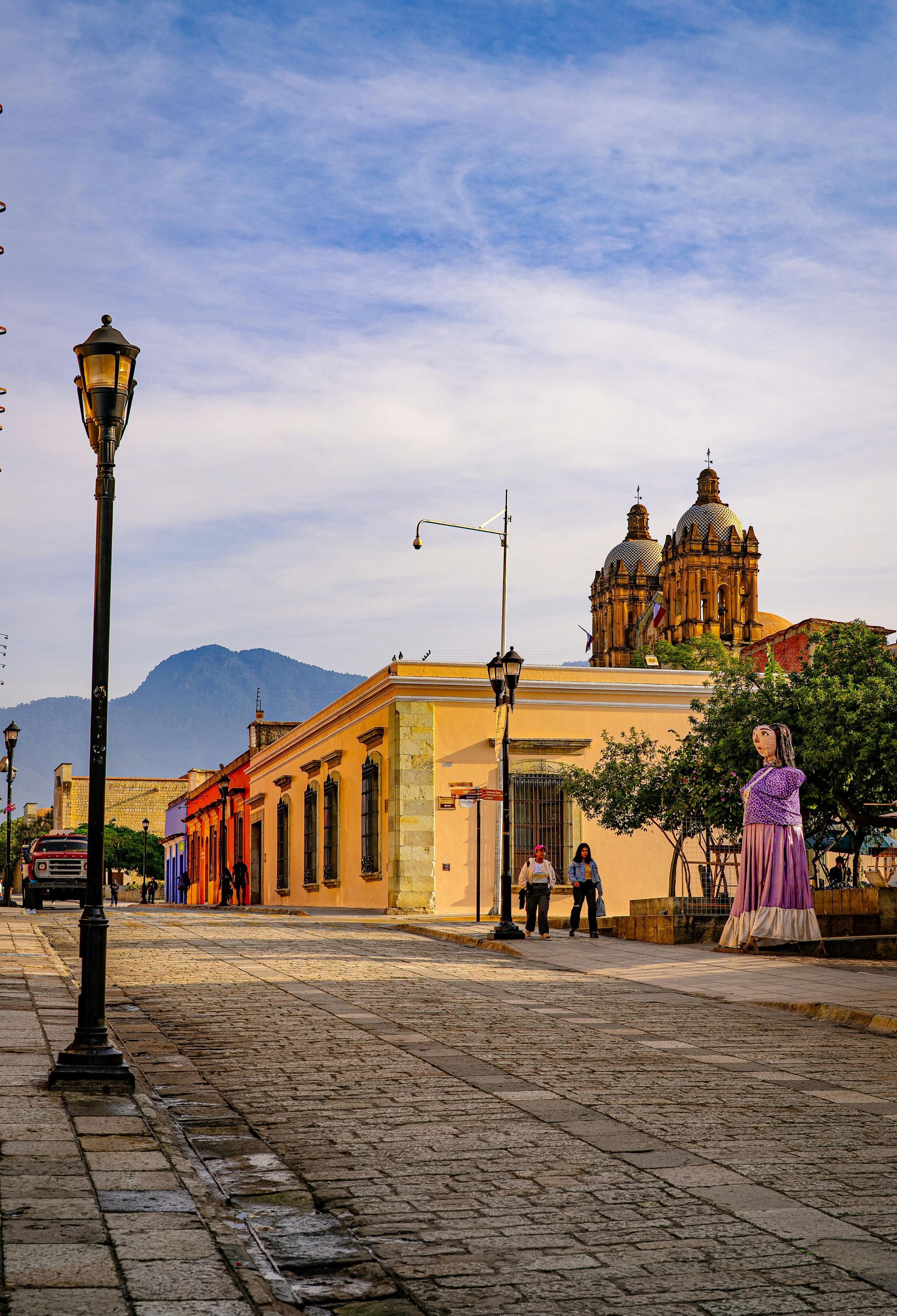 Una calle empedrada conduce a un edificio colonial amarillo con cúpulas de iglesia ornamentadas.