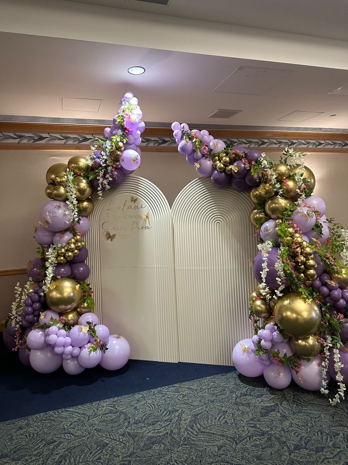 A room decorated with purple and gold balloons and flowers.