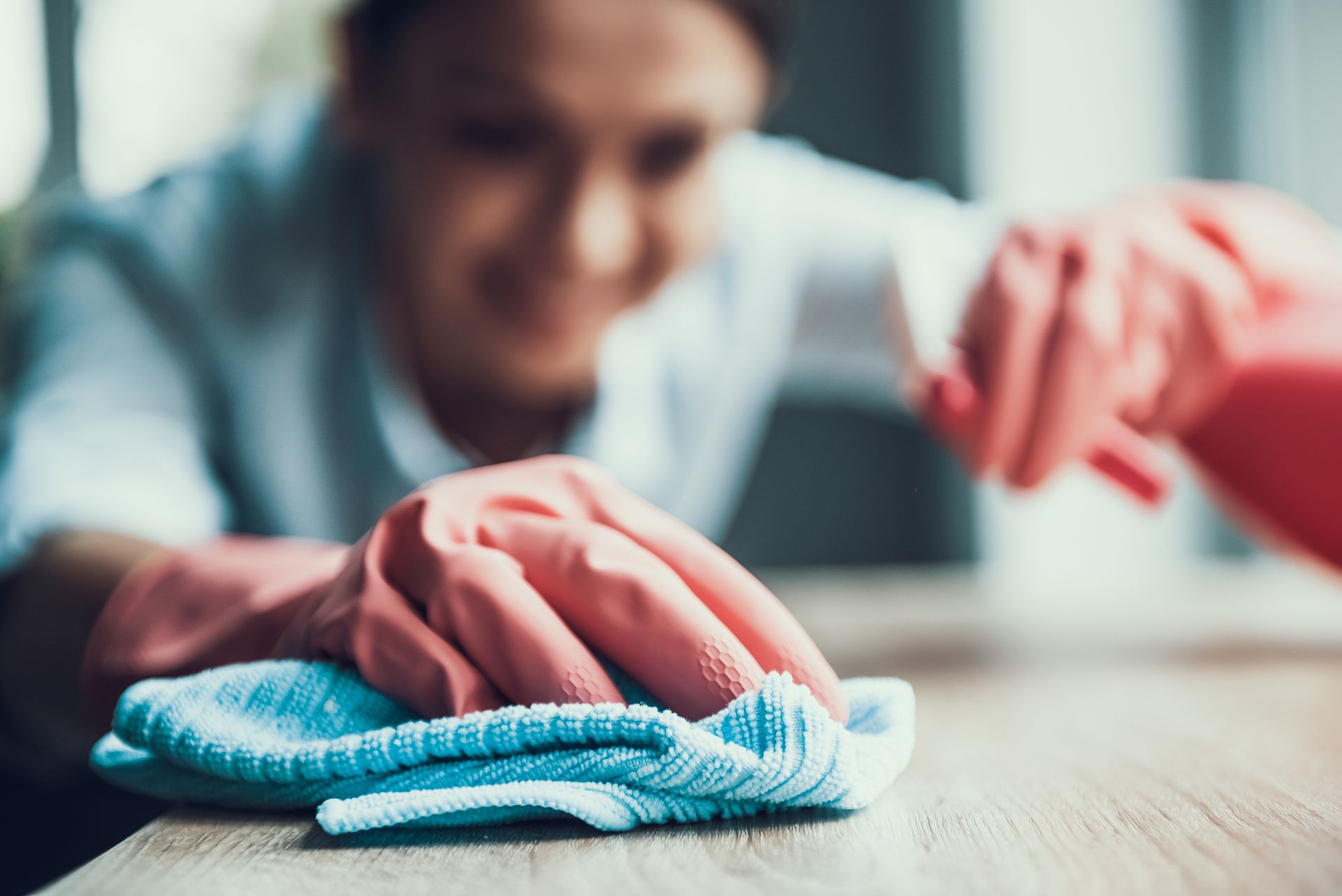 Person in pink gloves wiping a wooden surface with a blue cloth.