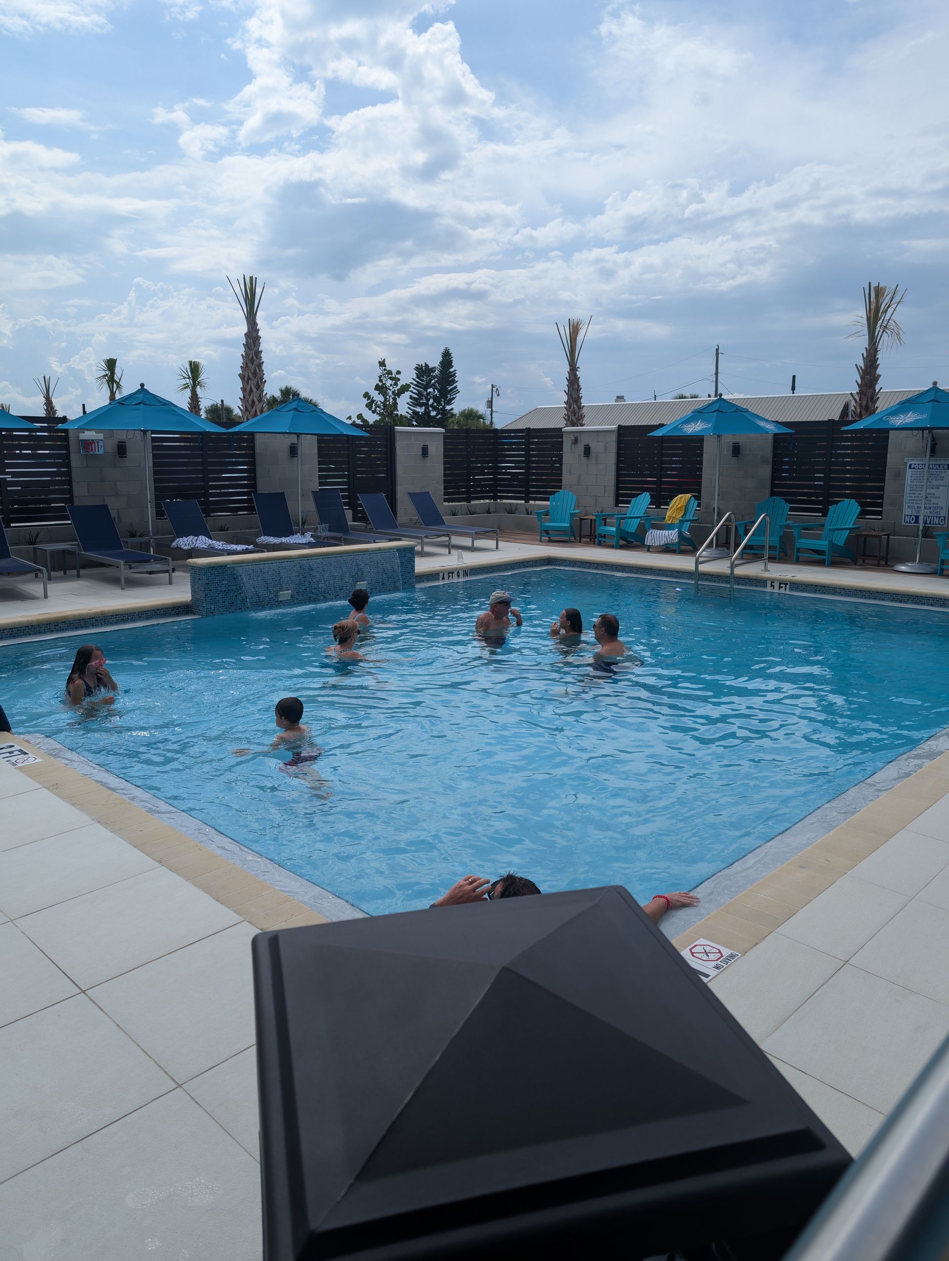Outdoor pool with swimmers, blue lounge chairs, and cabanas under a cloudy sky