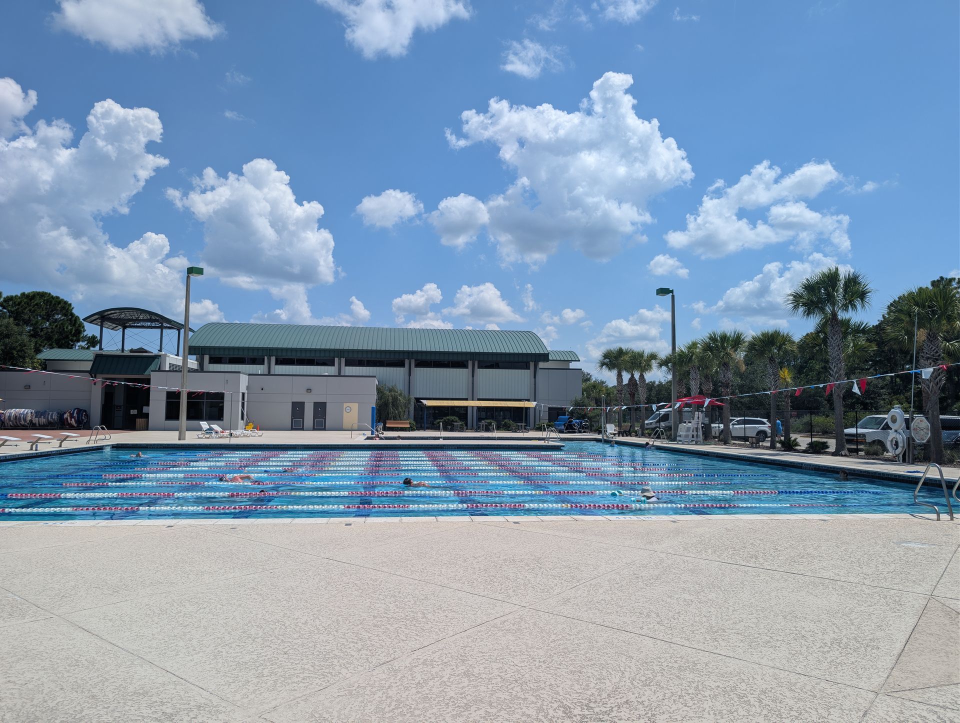 Outdoor swimming pool with colorful lanes under a bright blue sky and clouds