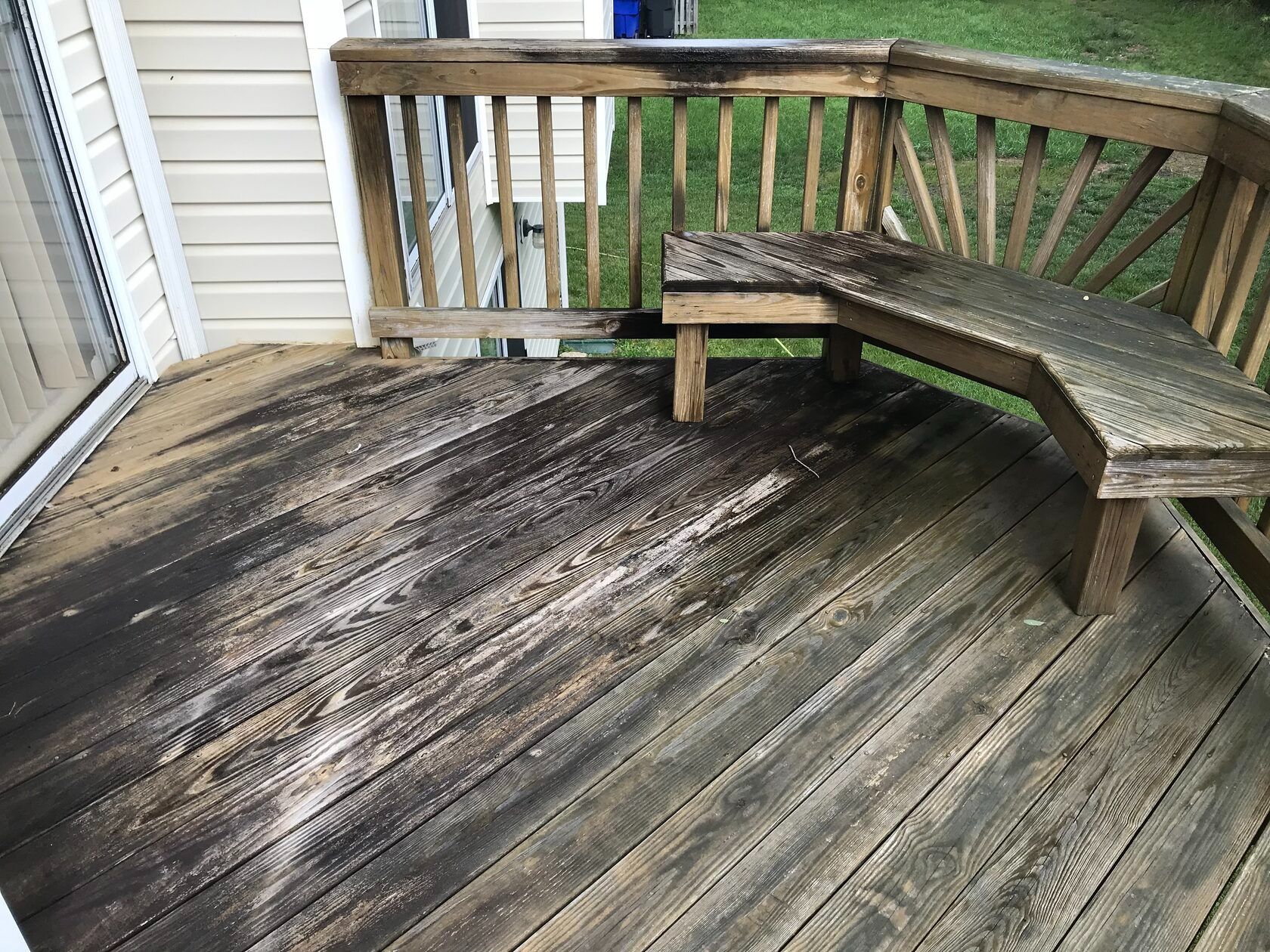 Weathered wooden deck with a built-in bench, appearing dirty and moldy. A railing borders the deck.