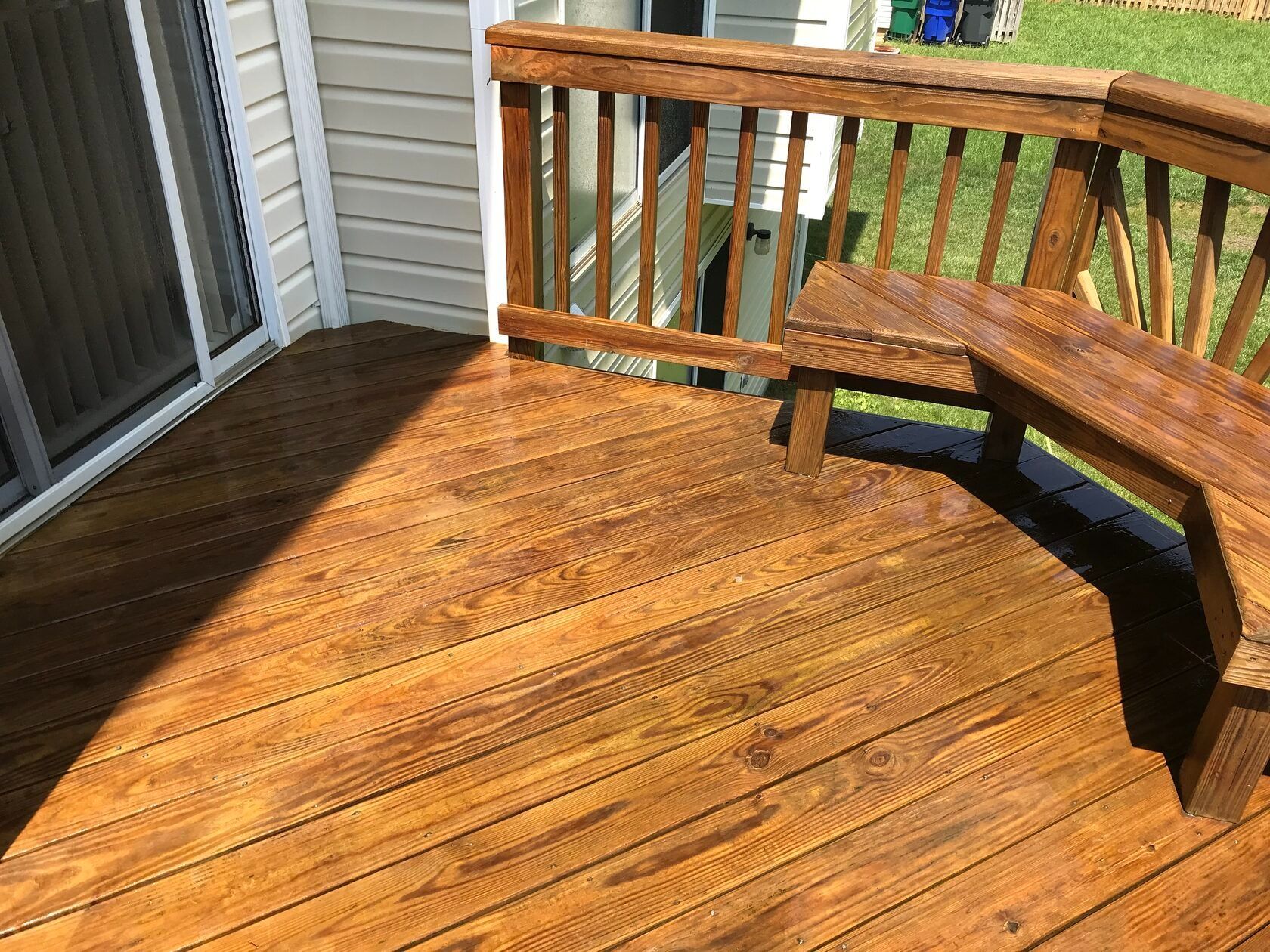Wooden deck with a stained finish and built-in bench. The deck is next to a sliding glass door and railing.