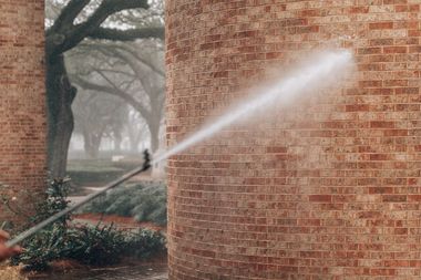 Pressure washing a brick column outdoors.