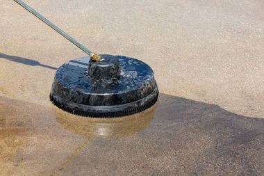 Pressure washer cleaning a light-colored concrete surface.