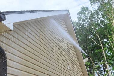 Pressure washing the beige siding of a house; water spraying.