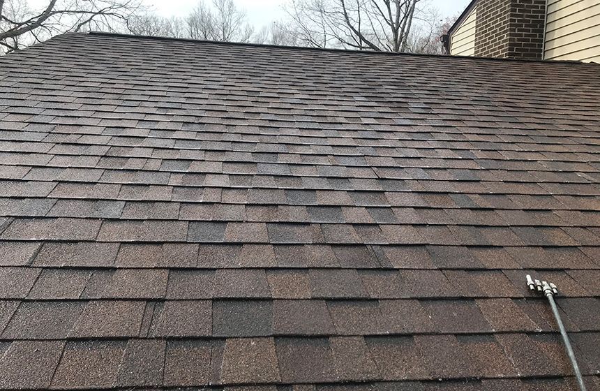 Brown shingle roof with a chimney in the background. Cloudy sky overhead.