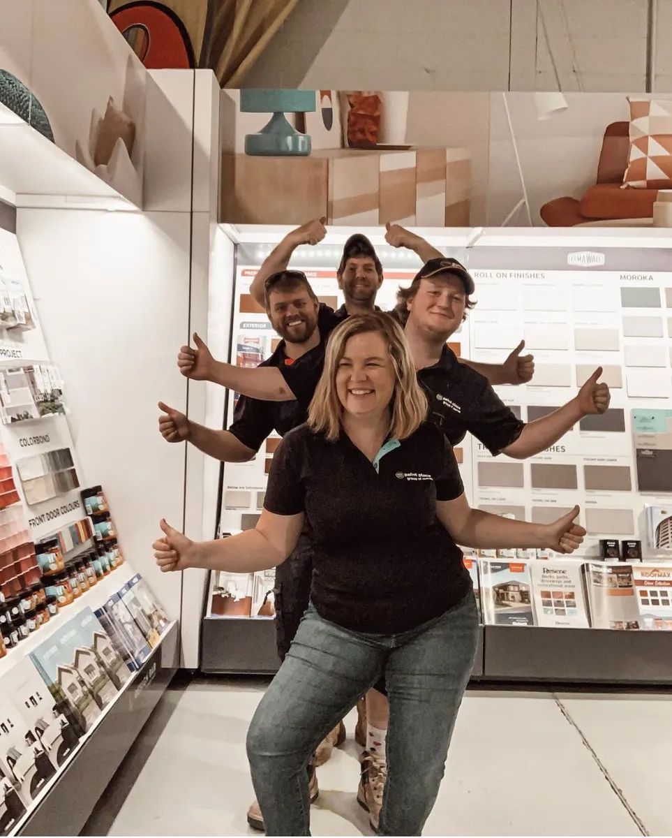 Four Smiling People Posing With Arms Outstretched in a Store Aisle — Paint Place Cowra in Cowra, NSW